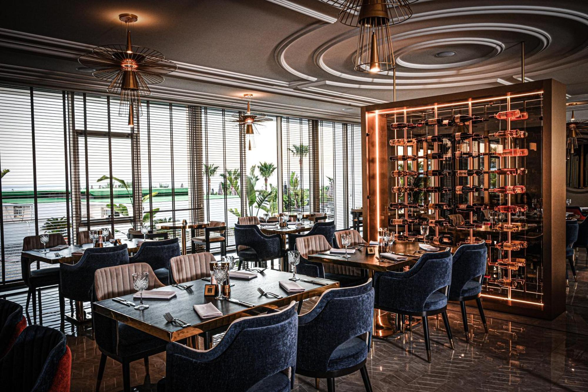 Acapulco Resort Hotel Agios Epiktitos Dış mekan fotoğraf The photo depicts a stylish and modern restaurant interior. It features a spacious dining area with large windows that let in natural light, creating an inviting atmosphere. The tables are set with elegant dinnerware, and there are plush blue chairs 