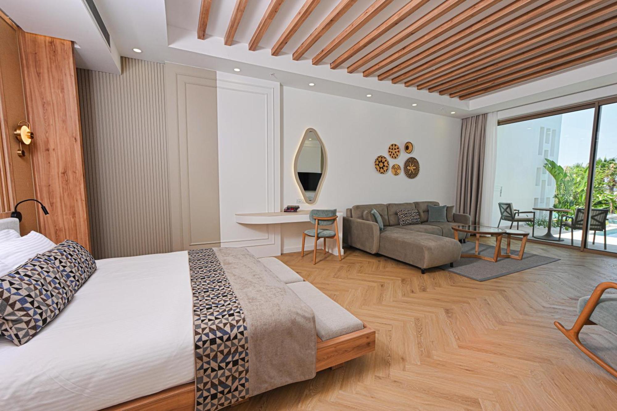 Acapulco Resort Hotel Agios Epiktitos Dış mekan fotoğraf The photo shows a modern hotel room that features a stylish design. On one side, there's a bed with a patterned throw blanket. Next to it, there's a small table and chairs, creating a cozy seating area. The room has a light wood ceiling with exposed 