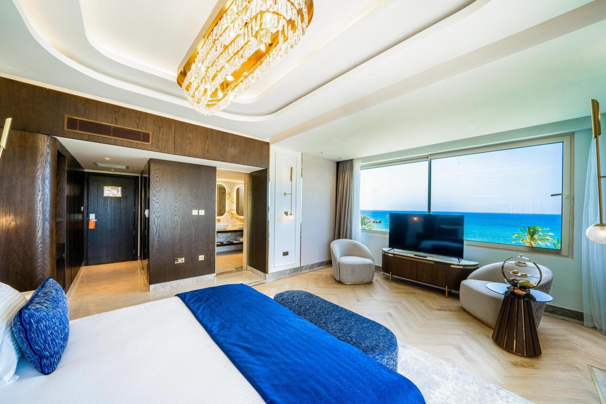 Acapulco Resort Hotel Agios Epiktitos Dış mekan fotoğraf The photo shows a modern hotel room with a spacious layout. It features a large bed with a blue throw blanket, a stylish chandelier hanging from the ceiling, and a comfortable seating area with armchairs. There's a flat-screen TV on a wooden stand an